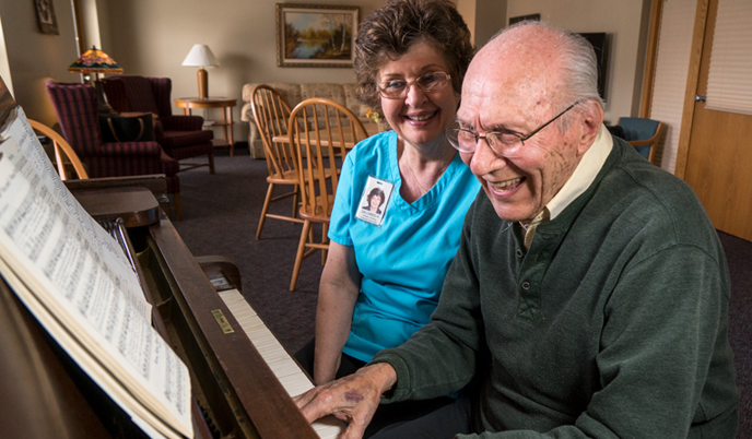 Two people sit at a piano at an assisted living facility