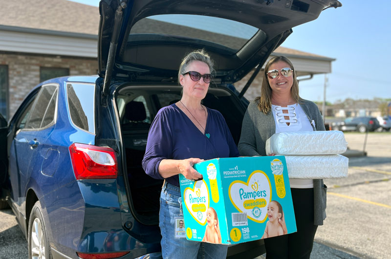 Karen Kinsman (left) and Julie Bluske stand outside a car with packages of diapers in their arms