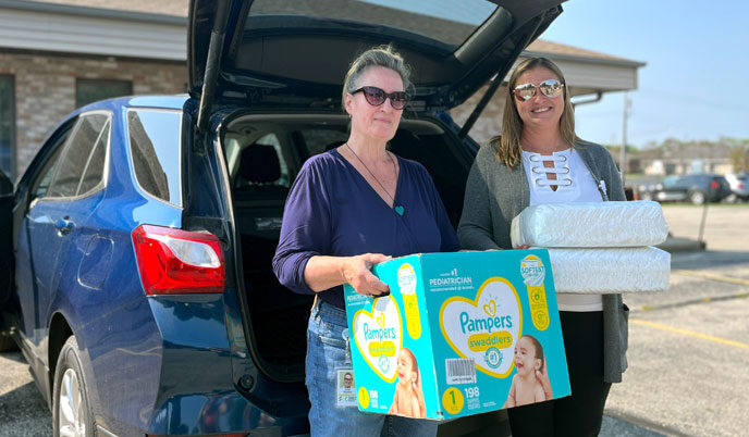 Karen Kinsman (left) and Julie Bluske stand outside a car with packages of diapers in their arms