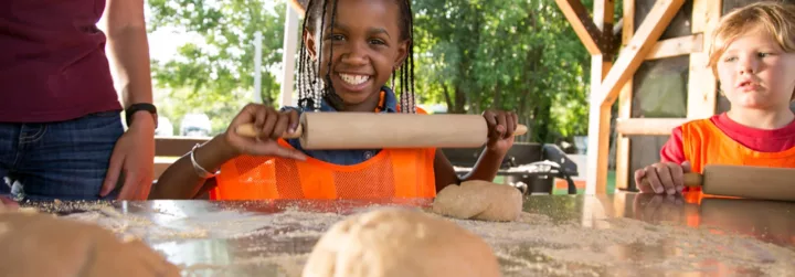 Smiling girl with a rolling pin and pizza dough