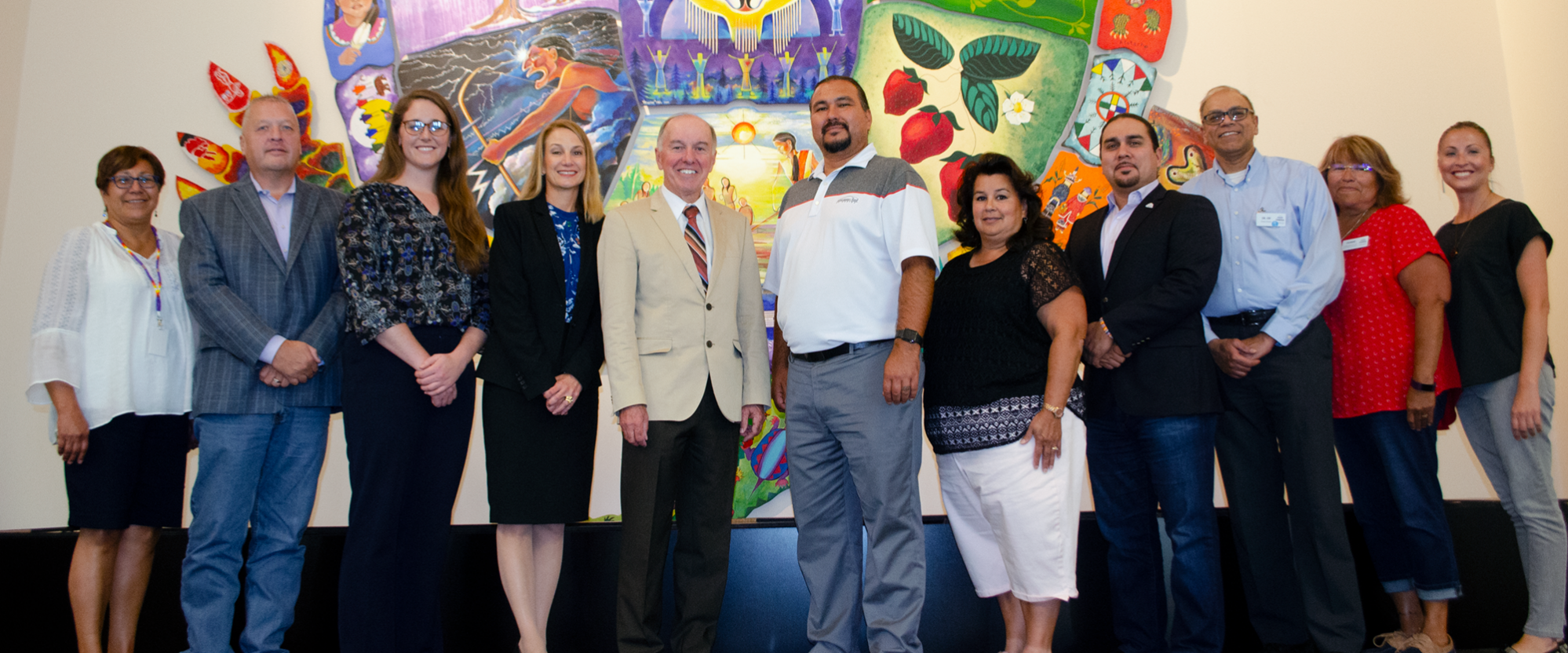 NACHP and Oneida Comprehensive Health Division teams stand smiling in front of a mural