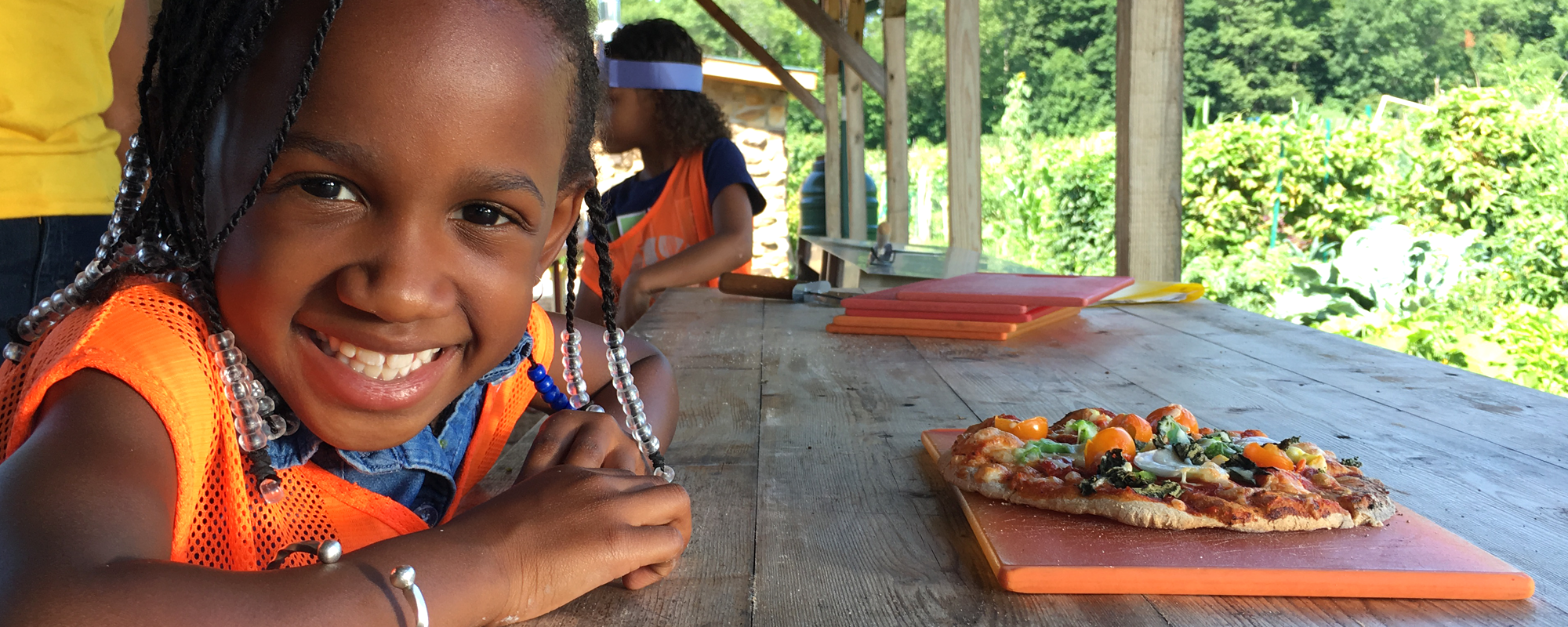 A girl smiles at a picnic table with a vegetable pizza on it