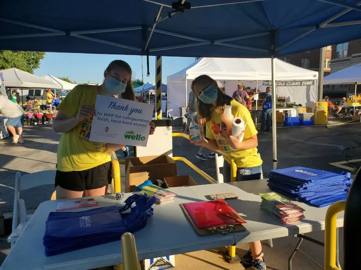 Farmer's market staff holding a thank you sign and cleaning supplies