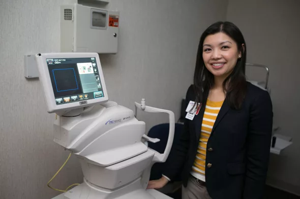 A doctor stands next to eye screening equipment